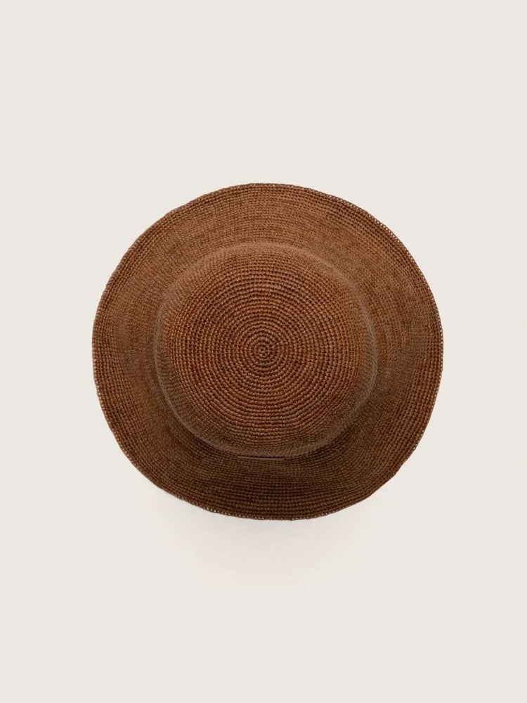 A brown woven straw hat viewed from directly above on a light off-white background.