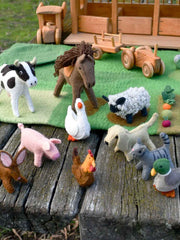Collection of toy animals on a wooden surface with a toy stable in the background