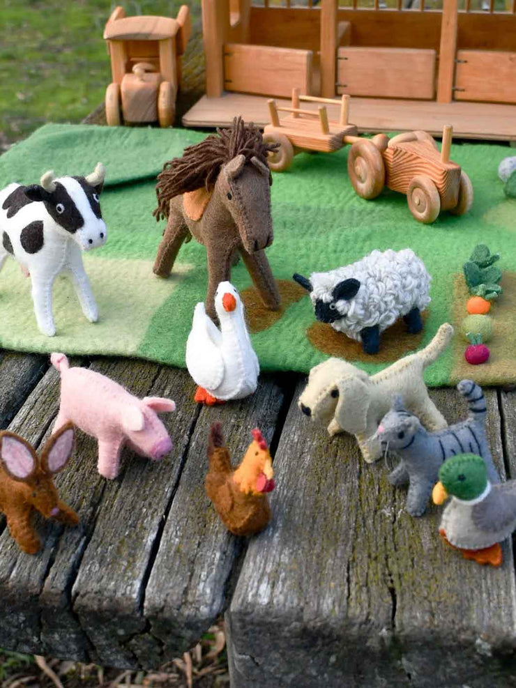 Collection of toy animals on a wooden surface with a toy stable in the background